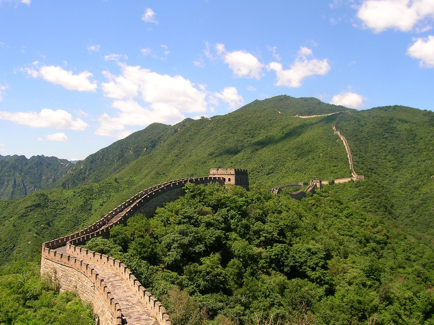 The Great Wall of China climbing a steep forested hillside under a blue sky