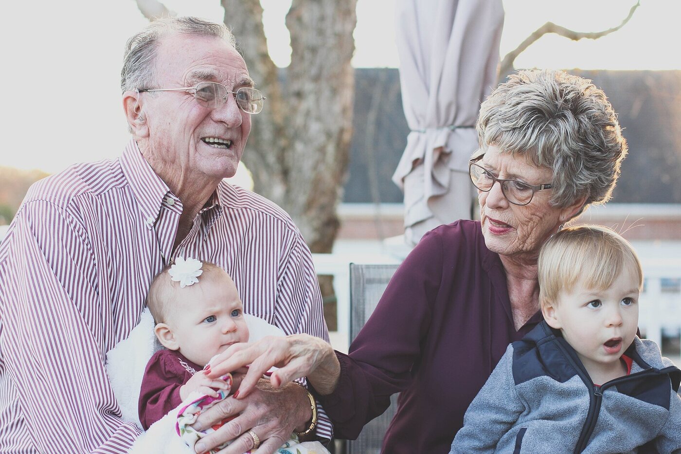 Smiling grandparents holding their two young grandchildren outdoors