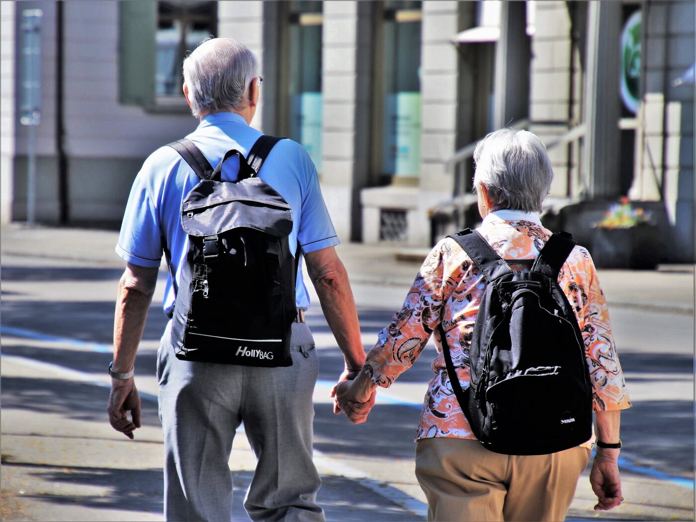 A retired couple holding hands while walking down a sunny street