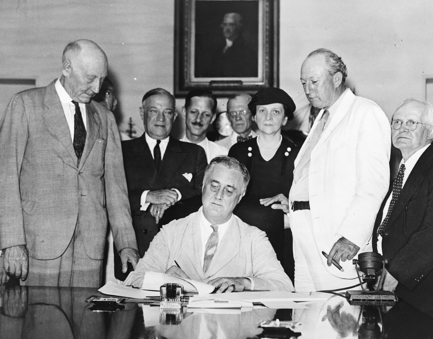President Franklin D. Roosevelt signing the Social Security Act at a desk surrounded by lawmakers in 1935