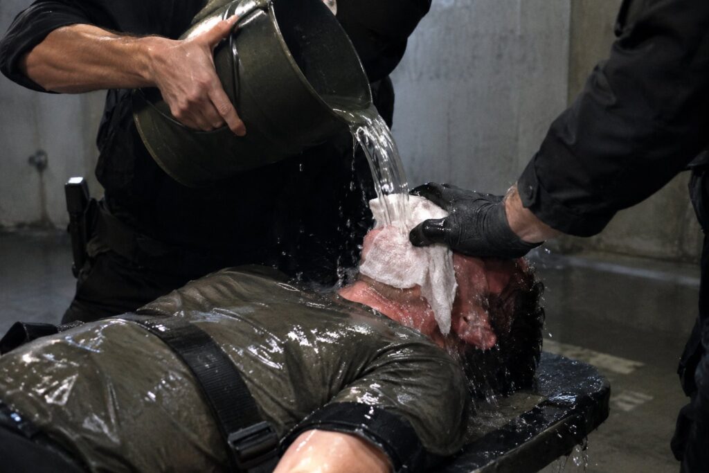 Staged illustration of a person on a bench having water poured over a cloth on their face, used as a metaphor for torturing numbers until they confess